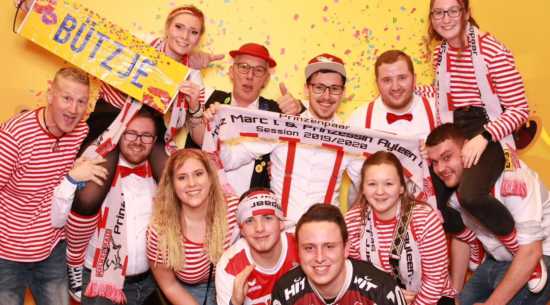 Gruppenfoto: Vereinsmitglieder in rot-weißen Kostümen feiern im Konfettiregen